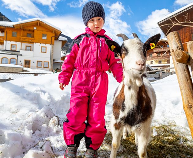 Ein Mädchen mit Schneeanzug steht neben einer Ziege im Schnee